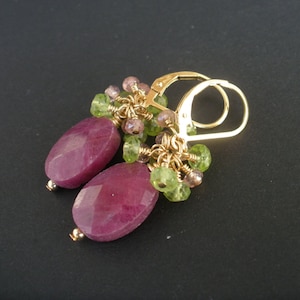 May include: Gold earrings with pink and green gemstone accents. The earrings feature two oval-shaped pink gemstones.