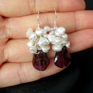 May include: A pair of dangle earrings with a cluster of white freshwater pearls and a teardrop-shaped, deep red gemstone.