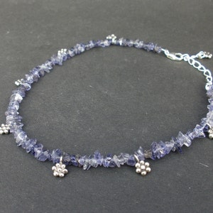 Può includere: Una collana d'argento con una catena delicata e piccole pietre di ametista sfaccettate. La collana ha una chiusura in argento e piccoli ciondoli a forma di fiore.