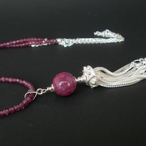 Puede incluir: Un collar de plata con un colgante de piedra preciosa rosa y un borla. El collar está hecho de pequeñas cuentas rosas y tiene una cadena de plata.