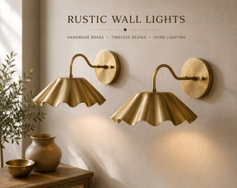 May include: Two brass wall lights with scalloped shades and curved arms. The text RUSTIC WALL LIGHTS, HANDMADE BRASS, TIMELESS DESIGN, HOME LIGHTING is visible above the fixtures. The lamps feature a circular wall mount and a metallic finish.