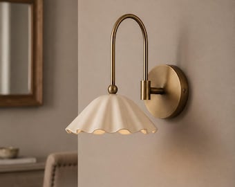 May include: A wall light featuring a curved brass arm and a circular brass wall mount. The fixture includes a scalloped, off-white ceramic shade. Text at the bottom reads: RUSTIC WALL LIGHTS, HANDMADE BRASS, TIMELESS DESIGN, HOME LIGHTING.