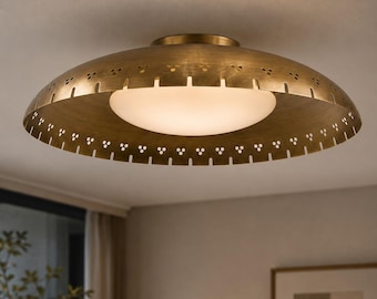 May include: A flush mount ceiling light fixture featuring a wide, circular brass-toned metal shade with a perforated edge pattern and a central, circular frosted white glass diffuser that emits a soft, warm glow across the room.