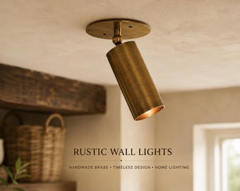 May include: A cylindrical brass spotlight fixture mounted to a circular ceiling plate with an adjustable swivel joint. The metal has a brushed finish. Text on the image reads: RUSTIC WALL LIGHTS, HANDMADE BRASS, TIMELESS DESIGN, HOME LIGHTING.
