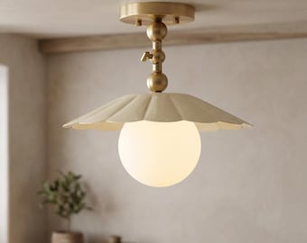 May include: A ceiling light fixture featuring a brass-toned metal stem with a central adjustment knob, a scalloped cream-colored metal shade, and a central spherical white glass globe that emits a soft, diffused light from within the fixture.