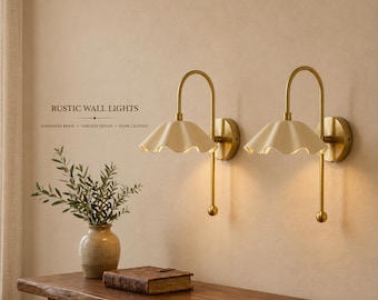 May include: Two wall-mounted lamps featuring curved brass arms and cream-colored, scalloped, petal-shaped shades. Each lamp has a circular wall plate and a vertical rod ending in a small sphere. The text RUSTIC WALL LIGHTS is visible.