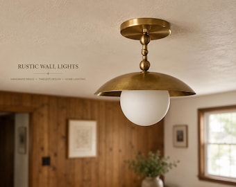 May include: A brass ceiling light fixture featuring a wide, shallow dome-shaped shade and a spherical white glass globe. The fixture is mounted with a central rod accented by two small spheres. Text on the image reads RUSTIC WALL LIGHTS.
