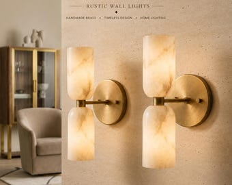 May include: Two wall lights featuring circular brass backplates and horizontal arms supporting two cylindrical, marbled stone shades each. The text RUSTIC WALL LIGHTS, HANDMADE BRASS, TIMELESS DESIGN, HOME LIGHTING is visible above the fixtures.