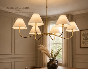May include: A six-light chandelier featuring a brass finish frame with curved arms and off-white fabric shades. The fixture is suspended from a central rod and ceiling canopy. Text in the image reads RUSTIC WALL LIGHTS HANDMADE BRASS TIMELESS DESIGN HOME LIGHTING.