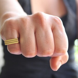 May include: A close-up of a hand wearing a gold ring with a stacked rectangular design.