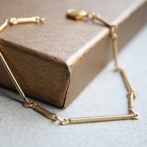 Puede incluir: Un brazalete de oro con un diseño geométrico. El brazalete está hecho de barras finas y rectas conectadas por pequeños anillos.