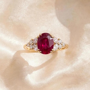 Könnte beinhalten: Ein Goldring mit einem großen, oval geschliffenen, tiefroten Rubin in der Mitte, flankiert von einer Gruppe aus drei marquise-geschliffenen, klaren weißen Diamanten auf jeder Seite, gefasst in eine polierte Gelbgoldschiene mit Krappenfassung.