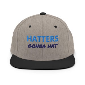 May include: A heather gray baseball cap with a black brim and a black top button. The front features embroidered text in blue and dark blue that reads HATTERS GONNA HAT. The cap has a structured six-panel design with black eyelets on each panel.
