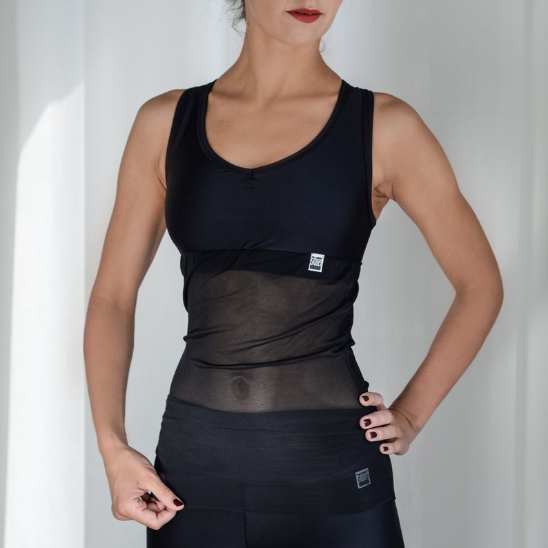 May include: Black tank top with a sheer mesh overlay and a black band at the bottom. The tank top has a scoop neck and a small logo on the front.