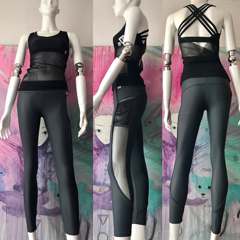 May include: A black mesh and solid athletic top with a criss-cross back detail, paired with dark gray leggings featuring a mesh panel on the left leg.