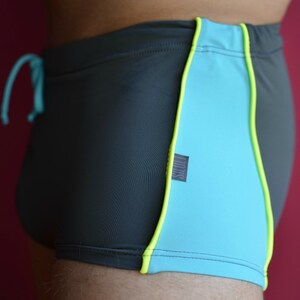 May include: Black swimming trunks with a turquoise and yellow trim. The trunks have a drawstring and a small label that says "FILIKS".