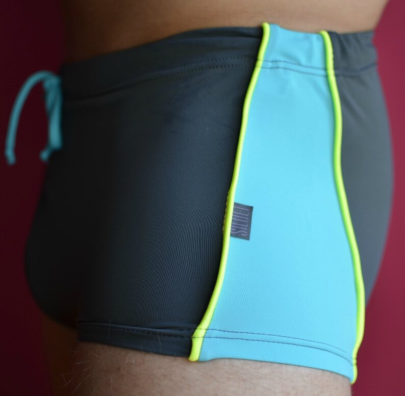 May include: Black swimming trunks with a turquoise and yellow trim. The trunks have a drawstring and a small label that says "FILIKS".