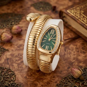 May include: A gold-tone quartz watch featuring a flexible, coiled snake-like band and a teardrop-shaped case. The watch face is dark green with gold Roman numeral markers and hands, surrounded by a bezel set with small, clear, sparkling stones.