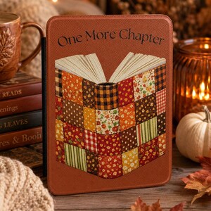 May include: A rectangular e-reader case with a textured rust-coloured surface. The front features the text One More Chapter above a graphic of an open book composed of a colourful patchwork quilt pattern in shades of orange, red, brown, and green.