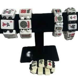 May include: Five bracelets constructed from white rectangular mahjong tiles featuring red, green, and black character and symbol engravings. The tiles are connected by small black beads, creating a flexible band structure for each individual bracelet.