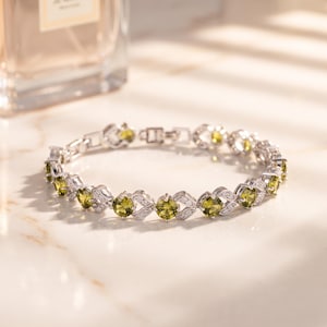 May include: A silver-toned link bracelet featuring a series of round-cut olive green gemstones alternating with small, clear, sparkling stones set in a decorative metal frame with a secure clasp mechanism.