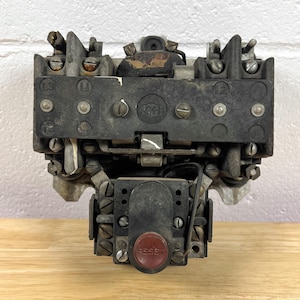 May include: A vintage industrial electrical motor starter featuring a black rectangular housing with visible L1, L2, L3, and T3 terminal markings. The unit includes a central GH logo and a prominent red circular button labeled RESET at the base.