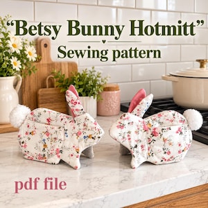 May include: Two rabbit-shaped hot mitts made of white fabric with a pink and green floral pattern. Each mitt features a white pom-pom tail and pink inner ears. The text "Betsy Bunny Hotmitt" and "Sewing pattern" appear above, with "pdf file" below.