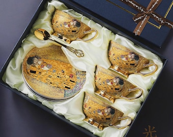 Puede incluir: Un juego de té en una caja de regalo azul oscuro con forro de satén, que incluye tres tazas de cerámica dorada y un platillo a juego, decorados con una reproducción del cuadro El Beso. Se incluye una cuchara de metal dorado en el set.