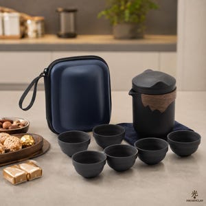 May include: A matte black tea set featuring a lidded teapot with a wooden accent, six matching small tea cups, and a dark blue zippered carrying case. The set is arranged on a surface alongside a wooden tray with small snacks and gold-wrapped items.