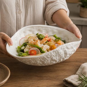 May include: A white ceramic bowl with an irregular, textured outer surface containing a salad of shrimp, asparagus, sliced radishes, and cherry tomatoes. The bowl has a smooth interior and a rough, organic-looking exterior finish.