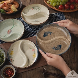 Puede incluir: Un juego de platos redondos de cerámica con un divisor central en forma de S. Cada plato tiene un diseño pintado a mano, incluyendo peces azules, motivos florales y ramas de sauce. Los platos tienen un acabado texturizado en beige y verde.