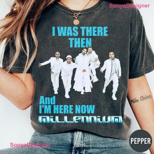 Pode incluir: Uma t-shirt de manga curta cinzento-carvão com um gráfico de uma boy band em fatos brancos. O texto diz I WAS THERE THEN And I'M HERE NOW MILLENNIUM em letras azul-brilhante. A t-shirt tem gola redonda e um aspeto vintage.