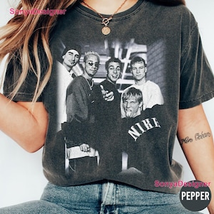 Pode incluir: Uma t-shirt de manga curta em cinzento-carvão com uma impressão gráfica vintage a preto e branco de uma boy band com quatro membros. Um membro veste uma peça com o texto NIKE impresso a branco na zona do peito da peça.