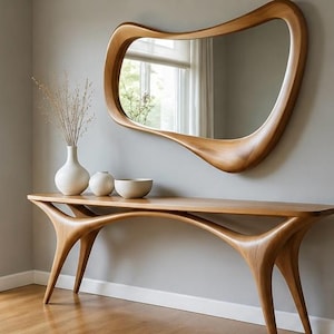 May include: A light brown wooden console table with curved, organic legs and a matching irregular, fluid-shaped wooden wall mirror. Two white ceramic vases and a white ceramic bowl are placed on the surface of the console table.