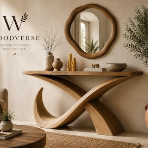Pode incluir: Uma mesa consola de madeira castanho-claro com uma base curva e entrecruzada. Sobre a mesa estão dois vasos de cerâmica, três velas de pilar amarelas, uma pilha de livros e uma taça. Acima está pendurado um espelho redondo irregular. Texto: W WOODVERSE CRAFTED BY NATURE, MADE FOR LIFE.