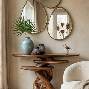 May include: A wooden console table with a twisted base and multiple tiered surfaces, featuring three asymmetrical gold-rimmed mirrors above it. On the table sit a light blue vase with a palm leaf, two small patterned vases, and a gold bird figurine.