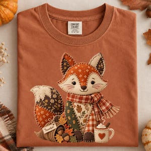 May include: A rust-coloured crew neck t-shirt featuring a graphic of a fox made of various patterned fabric patches. The fox wears a plaid scarf and sits next to a cornucopia with the text Thankful and a mug with a heart and steam.
