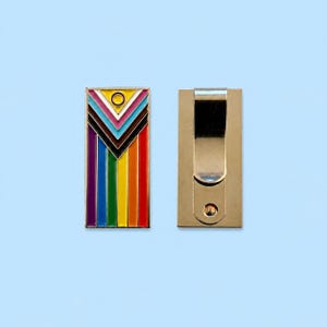 May include: A rectangular metal money clip featuring a colourful enamel design with vertical stripes in purple, blue, green, yellow, orange, and red, topped with a chevron pattern in white, pink, light blue, brown, and black, including a yellow circle.