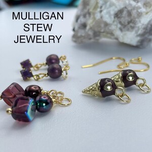 May include: Close-up of three pairs of earrings. One pair features purple beads and gold accents. Another pair has purple square gems and round beads. The third pair is ice cream cone shaped with gold and purple details. The text "MULLIGAN STEW JEWELRY" is at the top.