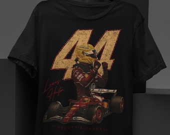 Puede incluir: Una camiseta negra de manga corta con un gráfico grande de un coche de Fórmula 1 y un piloto con casco amarillo. El número 44 está impreso en una fuente dorada desgastada sobre el coche, con el texto Lewis Hamilton y Scuderia Ferrari.