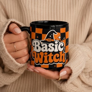 May include: A black ceramic mug featuring an orange and black checkerboard pattern. The front displays a black witch hat icon above the white and orange text "Basic Witch" in a retro font, accented with small white star shapes throughout the design.