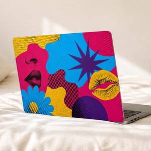 May include: A laptop skin featuring a vibrant pop art design with a bright blue background, a pink silhouette of a face, a yellow pair of lips, a blue flower, a dark purple starburst, and a black and pink checkered pattern with halftone dots.