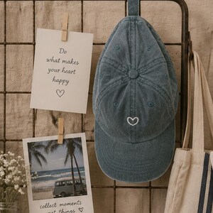 Peut inclure: Une casquette de baseball en jean bleu avec un petit cœur blanc brodé sur le panneau avant. La casquette présente une calotte structurée avec un bouton sur le dessus et une visière incurvée. Le tissu a un aspect délavé et légèrement usé.