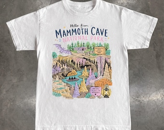 May include: A white short-sleeve t-shirt featuring a colorful graphic print that reads Hello from MAMMOTH CAVE NATIONAL PARK. The illustration depicts a cave interior with stalactites, a river with a boat, a bat, a lantern, and text reading NATURE IS FULL OF WONDERS.