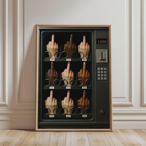 May include: A framed wall art print depicting a dark grey vending machine with a glass front. Inside, nine slots labelled A1 through D3 each contain a hand making a middle finger gesture. The machine features a digital display reading 5000.