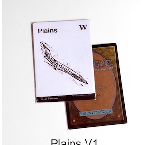 May include: A white Magic: The Gathering Plains card featuring a minimalist black ink illustration of a landscape, the text Plains, and a W symbol. Partially underneath is a second card showing the classic brown and orange card back design.