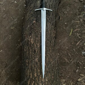 May include: A double-edged steel sword featuring a long, tapered blade with a central fuller, a straight silver-toned crossguard, a black leather-wrapped grip, and a round, polished silver-toned pommel at the end of the handle.