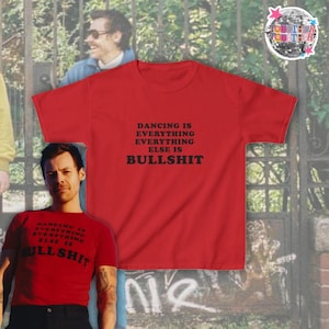 Könnte beinhalten: Ein leuchtend rotes Kurzarm-T-Shirt mit schwarzem Text auf der Vorderseite, der lautet: DANCING IS EVERYTHING EVERYTHING ELSE IS BULLSHIT. Das T-Shirt hat einen klassischen Rundhalsausschnitt und eine Standardpassform mit fetter Schrift.