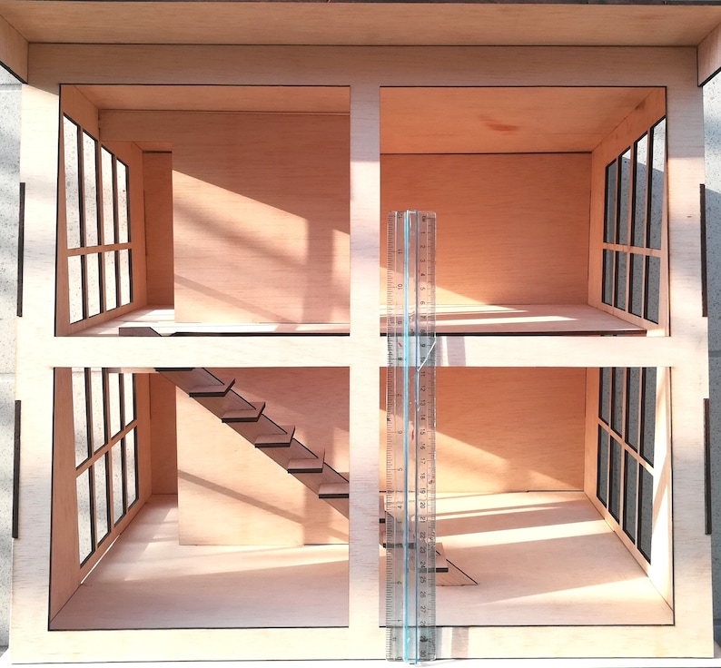 K&ouml;nnte beinhalten: Ein Holzpuppenhaus mit zwei Etagen, jede mit einem Raum und einem Fenster. Die untere Etage hat eine Treppe, die zur oberen Etage f&uuml;hrt. Ein Lineal ist vor dem Puppenhaus platziert.