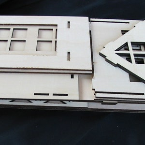K&ouml;nnte beinhalten: Ein Satz unfertiger Holzst&uuml;cke zum Bau eines kleinen Hausmodells. Die Teile sind gestapelt und beinhalten ein Dach, W&auml;nde und Fenster.